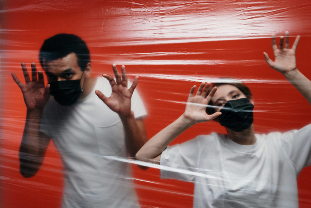 Personnes portant un masque anti-virus et se tenant derrière un mur de cellophane